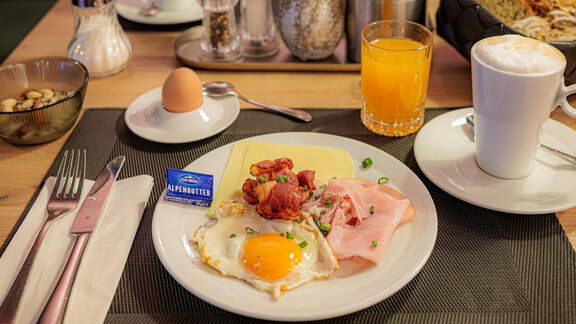 Ein schöner Frühstückstisch mit einem Teller voller Rührei, Schinken und Bacon. Dazu gibt es einen Softdrink, Kaffee und frisches Gebäck. - Bäckelar Wirt - Sölden