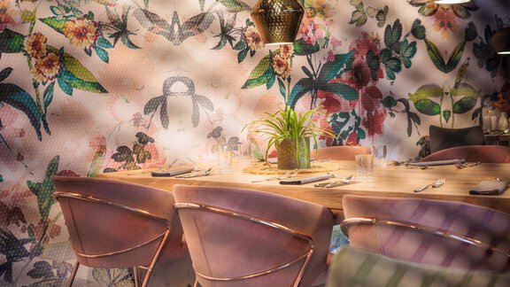 Ein modernes Restaurant mit einem blumigen Wanddesign. Die Tische sind elegant gedeckt und von stilvollen Lampen beleuchtet. - Bäckelar Wirt - Sölden