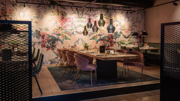 Ein stilvoller Essbereich mit einem großen Tisch und modernen Stühlen. Die Wände sind mit floralen Motiven und dekorativen Lampen geschmückt. - Bäckelar Wirt - Sölden