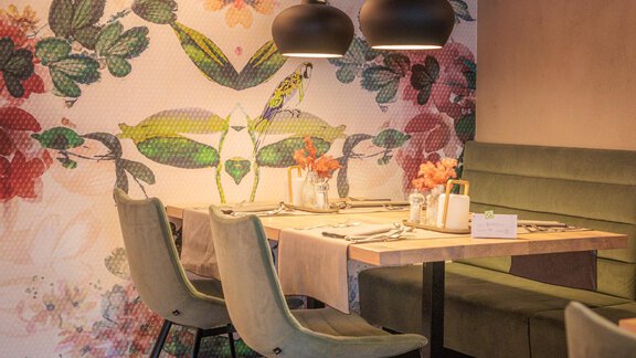 Ein modernes Restaurant mit einer schönen Wanddekoration aus Blumenmotiven. Die Tische sind elegant gedeckt und mit stilvollen Lichtquellen ausgestattet. - Bäckelar Wirt - Sölden