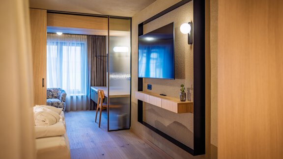 Ein modernes Zimmer mit einem Fernseher und einem gemütlichen Sessel. Das warme Holzdesign schafft eine einladende Atmosphäre. - Bäckelar Wirt - Sölden