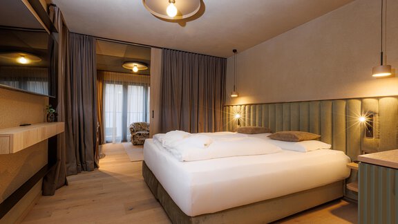Ein modernes Hotelzimmer mit einem großen Bett und warmen Farben. Große Fenster und stilvolle Beleuchtung schaffen eine gemütliche Atmosphäre. - Bäckelar Wirt - Sölden