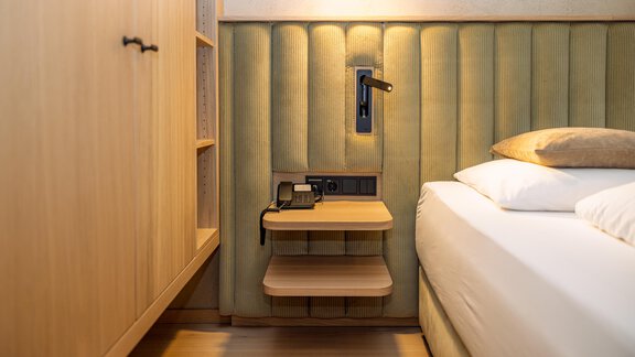 Ein modernes Schlafzimmer mit einem gepolsterten Kopfteil und einer bequemen Bettdecke. Neben dem Bett befindet sich ein geschmackvoller Nachttisch mit einer Lampe und Steckdosen. - Bäckelar Wirt - Sölden