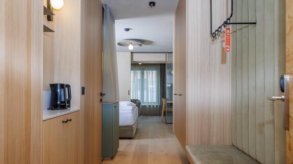 Ein moderner Eingangsbereich mit Holzverkleidung und klaren Linien. Sicht auf ein gemütliches Zimmer mit Fenster im Hintergrund. - Bäckelar Wirt - Sölden