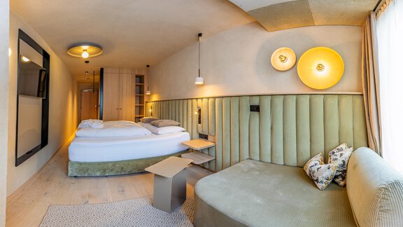 Ein modernes Hotelzimmer mit einem gemütlichen Bett und einem Sitzbereich. Die warmen Farben und das zeitgemäße Design schaffen eine einladende Atmosphäre. - Bäckelar Wirt - Sölden