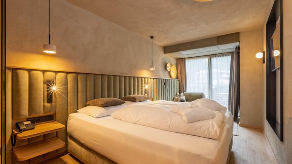 Ein modernes Schlafzimmer mit einem großen Bett und sanfter Beleuchtung. Große Fenster sorgen für viel Tageslicht. - Bäckelar Wirt - Sölden