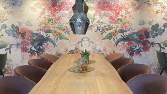 Ein moderner Essbereich mit einem großen Holztisch und bequemen, rosafarbenen Stühlen. Die Wände sind mit einem bunten Blumenmuster dekoriert. - Bäckelar Wirt - Sölden