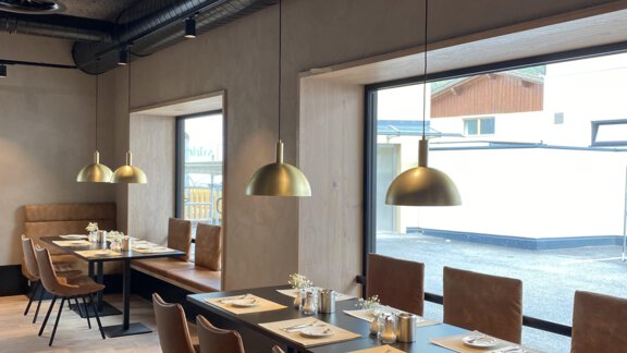 Ein modernes Restaurant mit eleganten Tischen und Stühlen. Große Fenster sorgen für viel Tageslicht und eine angenehme Atmosphäre. - Bäckelar Wirt - Sölden