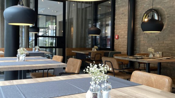 Ein modernes Restaurant mit Holztischen und eleganten Leuchten. Die Tische sind mit grauen Tischdecken und Vasen dekoriert. - Bäckelar Wirt - Sölden