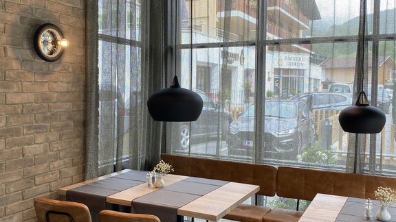 Ein modernes Café mit großen Fenstern und stilvollen Holztischen. Die Einrichtung ist schlicht und einladend, mit goldenen Dekorationen. - Bäckelar Wirt - Sölden