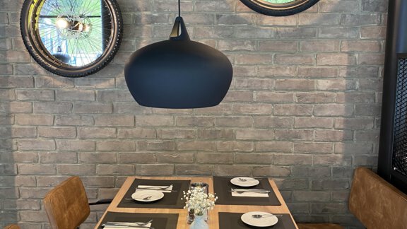 Ein stilvolles Restaurant mit einer Holztafel und modernen Stühlen. An der Wand hängen runde Spiegel und eine elegante Lampe hängt über dem Tisch. - Bäckelar Wirt - Sölden