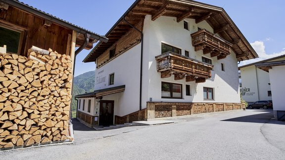A modern mountain house with traditional wooden design and balconies. In the foreground, there is a stack of wood. - Belledonne Ski in & out Appartements - Sölden