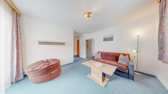 A cozy living space with a sofa, a table, and a beige bean bag. Large windows let in plenty of light and create a bright atmosphere. - Belmonte Sölden - Sölden