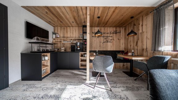 A modern living room with wooden walls and an open kitchen area. There is a dining table, chairs, and cozy seating. - Bianca`s BB - Sölden