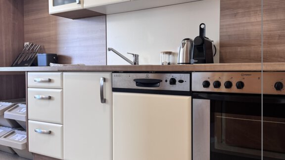 A modern kitchen with wooden and white cabinets. It is equipped with a stove, a dishwasher, and other kitchen appliances. - CASA bianco DUE - Sölden