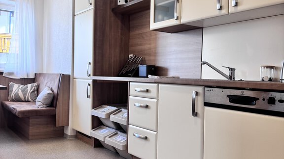 A modern kitchen with wooden and white cabinets. In the corner, there is a cozy sofa area. - CASA bianco DUE - Sölden