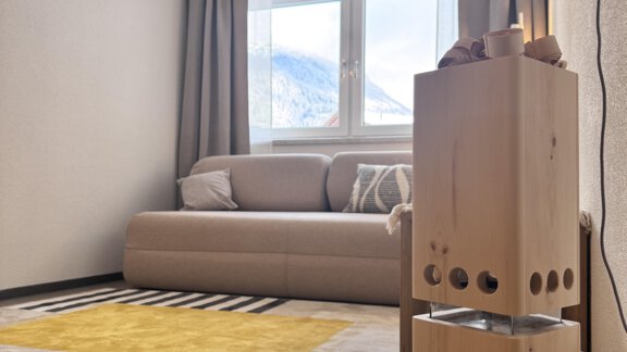 A cozy living room with a gray sofa and a yellow rug. The room has large windows that let in plenty of natural light. - CASA bianco DUE - Sölden