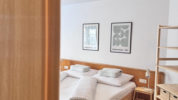 A cozy bedroom with a double bed and elegant wooden nightstand furniture. Two pictures hang on the wall and the floor is decorated with a carpet. - CASA bianco DUE - Sölden