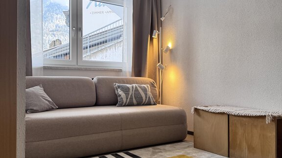 A modern room with a beige sofa and a yellow carpet. Large windows provide plenty of daylight. - CASA bianco DUE - Sölden