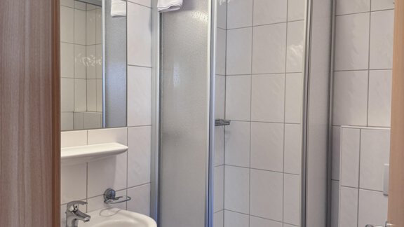A modern bathroom with a shower and a sink. The walls are tiled and the floor is blue. - CASA bianco DUE - Sölden