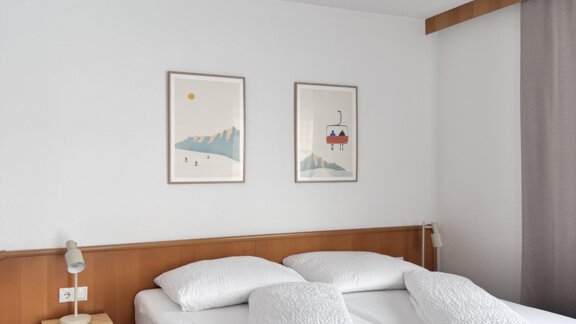 A cozy bedroom with a double bed and two large pillows. Pictures hang on the walls, and there is a bedside table with a lamp. - CASA bianco DUE - Sölden