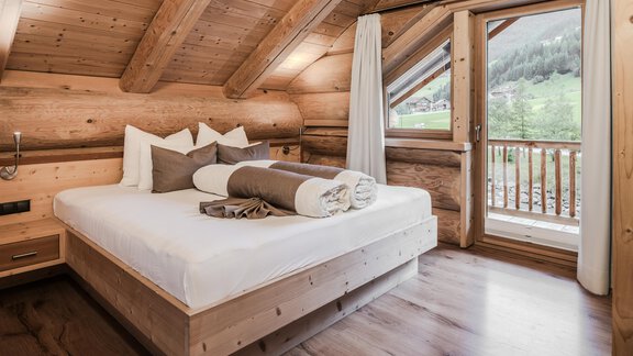 A cozy bedroom with wooden paneling and large windows. The room is furnished with a double bed and fresh towels. - Chalet Resort Sölden - Sölden