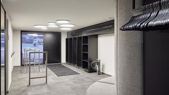 A modern entrance area with minimalist furnishings. It includes a seating area, a coat rack, and large windows that provide natural light. - Chalet White Pearl by MYALPS - Sölden