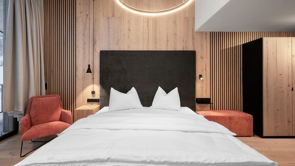 A modern bedroom with a large bed and a stylish headboard. The wooden paneling and warm colors create a cozy atmosphere. - Chalet White Pearl by MYALPS - Sölden