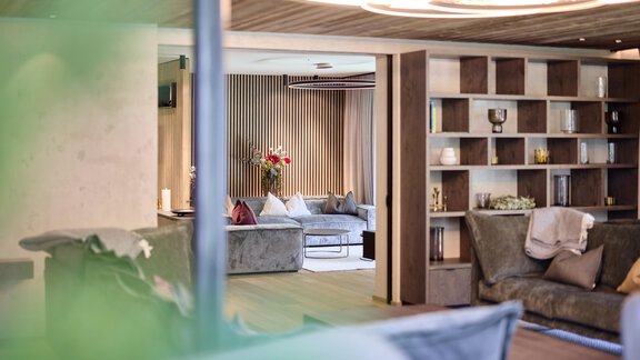 A modern living room with comfortable sofas and a bookshelf. Soft lighting creates an inviting atmosphere. - Chalet White Pearl by MYALPS - Sölden