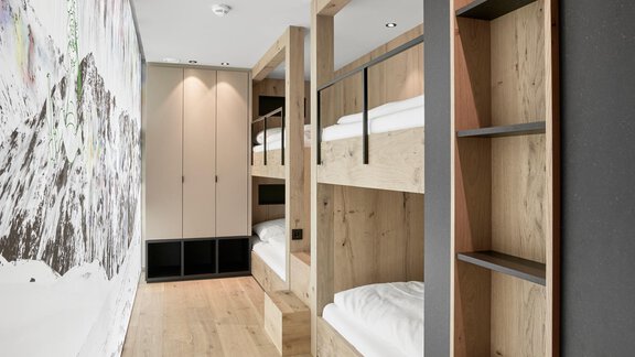 A modern room with wooden beds and a light wooden floor. The walls are plain and there is plenty of space for storage. - Chalet White Pearl by MYALPS - Sölden
