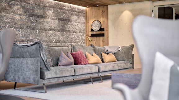 A stylish living room with a comfortable gray sofa and colorful cushions. The modern atmosphere is accentuated by the wooden ceiling and the simple wall design. - Chalet White Pearl by MYALPS - Sölden