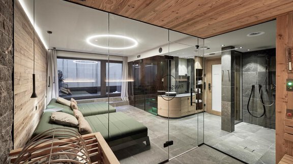 A modern wellness area with glass walls, green loungers, and a modern shower. The room is bright and inviting, perfect for relaxing. - Chalet White Pearl by MYALPS - Sölden