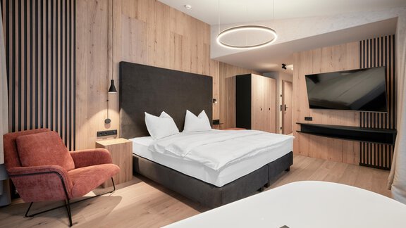 A modern bedroom with a comfortable bed and wood paneling. A cozy seating area and a large television complement the stylish atmosphere. - Chalet White Pearl by MYALPS - Sölden