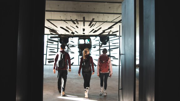 Three people walk through a modern door into a bright room. An artistic wall design is visible in the background. - Chalet White Pearl by MYALPS - Sölden