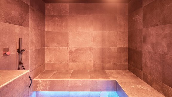 A modern wellness area with a small sauna and a blue water basin. The walls are made of gray tiles and softly lit. - Chalet White Pearl by MYALPS - Sölden