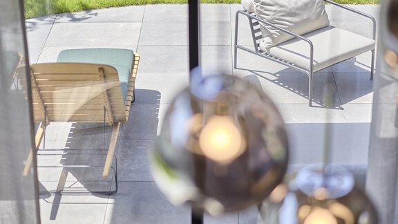 A view out the window onto a terrace with modern furniture. The lawn in the background is green and inviting. - Chalet White Pearl by MYALPS - Sölden