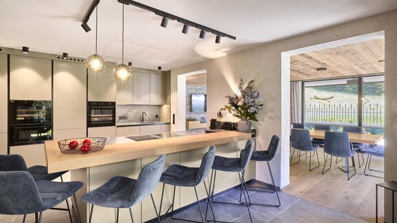 A modern kitchen with a large wooden dining table and stylish chairs. The room has plenty of light and a view of the outdoors. - Chalet White Pearl by MYALPS - Sölden