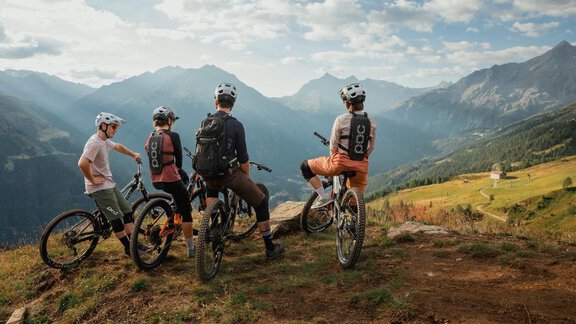 Four cyclists are standing on a mountain and looking into the distance. In the background, impressive mountain landscapes and a clear sky can be seen. - Chalet White Pearl by MYALPS - Sölden