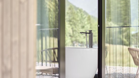 A modern bathroom with a freestanding bathtub and large windows. The beautiful nature in the background is visible through the glass doors. - Chalet White Pearl by MYALPS - Sölden