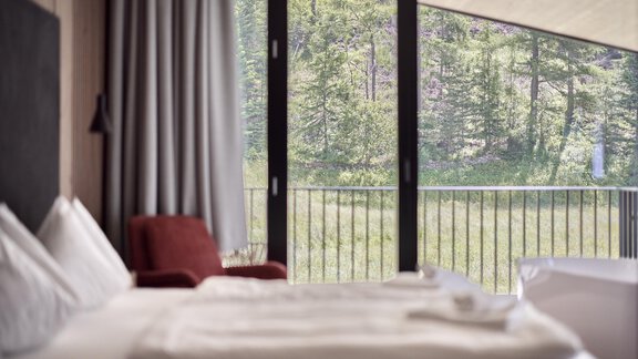 A modern hotel room with a view of the green trees outside. The room is bright and cheerfully furnished. - Chalet White Pearl by MYALPS - Sölden