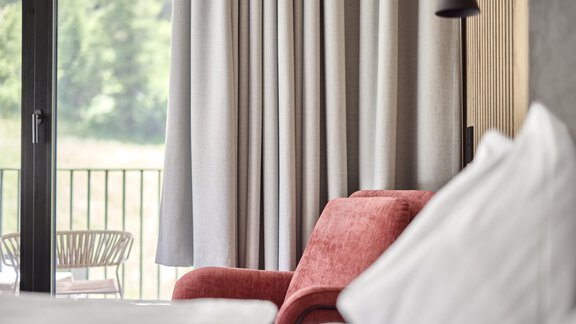 A modern room with a red armchair and elegant curtains. In the background, a balcony is visible, providing a view to the outside. - Chalet White Pearl by MYALPS - Sölden
