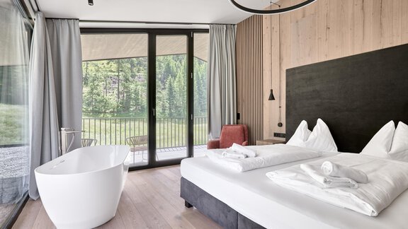 A modern bedroom with wood paneling and large windows. There is a comfortable double bed and a freestanding bathtub. - Chalet White Pearl by MYALPS - Sölden