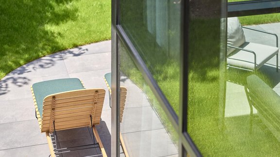A modern patio seat overlooking a green lawn. The glass walls of the building reflect the light and create a bright atmosphere. - Chalet White Pearl by MYALPS - Sölden