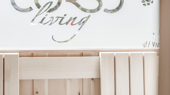A bright sauna with a wooden bench and white towels. In the background, there is a transparent window with the inscription "CORSO living" visible. - CORSO living Aparthotel - Sölden