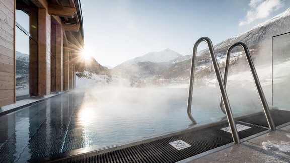 Ein beheizter Außenpool mit Blick auf verschneite Berge. Die Sonne scheint durch den Dampf des Wassers. - Das Central - Alpine . Luxury . Life - Sölden
