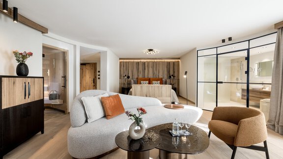 Ein modernes Hotelzimmer mit einem komfortablen Sofa und einem eleganten Tisch. Der Raum ist hell und großzügig geschnitten, mit einer klaren Glaswand, die einen Blick auf den Schlafbereich bietet. - Das Central - Alpine . Luxury . Life - Sölden