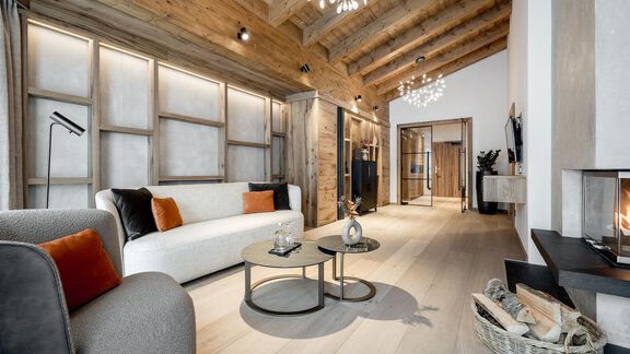 Ein modernes Wohnzimmer mit Holzstrahlen und einem gemütlichen Kamin. Es gibt einen hellen Sofa, einen Sessel und stilvolle Tischdekorationen. - Das Central - Alpine . Luxury . Life - Sölden