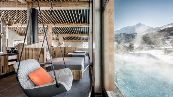 Moderne Inneneinrichtung mit schwebendem Stuhl und großem Fenster. Blick auf einen dampfenden Pool und die Berge im Hintergrund. - Das Central - Alpine . Luxury . Life - Sölden