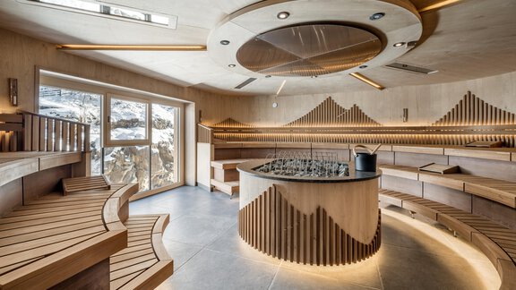 Ein eleganter Wellnessbereich mit Holzverkleidungen und einem zentralen Bereich für Getränke. Große Fenster bieten einen Blick auf die umliegenden Berge. - Das Central - Alpine . Luxury . Life - Sölden