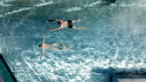 Zwei Personen schwimmen entspannt in einem klaren Pool. Die Wasseroberfläche reflektiert das Licht und schafft eine ruhige Atmosphäre. - Das Central - Alpine . Luxury . Life - Sölden